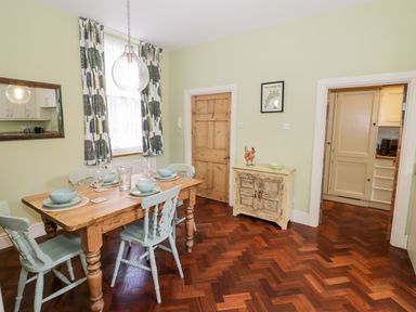 A dining room with a wooden table set for four with light blue chairs and patterned curtains at 4 The Old Council House in Shipston-On-Stour