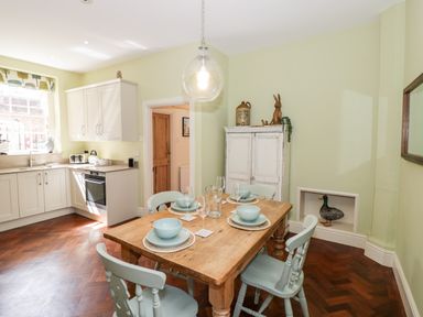 A kitchen with a wooden dining table set for four and white cabinets at 4 The Old Council House Shipston-On-Stour