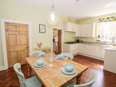 A kitchen with a wooden dining table set for four and pale green chairs at 4 The Old Council House in Shipston-On-Stour