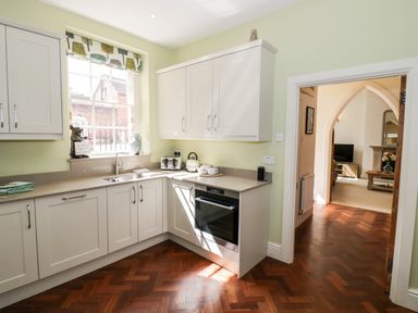 A kitchen with white cabinets a window a sink a toaster a kettle and an oven with a view into a living room at 4 The Old Council House in Shipston-On-Stour