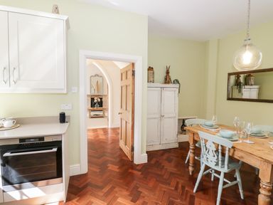 A dining area with a wooden table set with bowls and glasses next to a white cabinet and kitchen appliances at 4 The Old Council House in Shipston-On-Stour