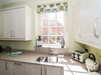 A kitchen with a sink under a window and white cabinets at 4 The Old Council House in Shipston-On-Stour