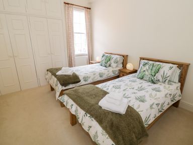 A bedroom with two single beds with green leaf patterned bedding and towels on the beds at 4 The Old Council House in Shipston-On-Stour