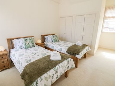 A bedroom with two single beds with green leaf patterned bedding and wooden nightstands at 4 The Old Council House in Shipston-On-Stour
