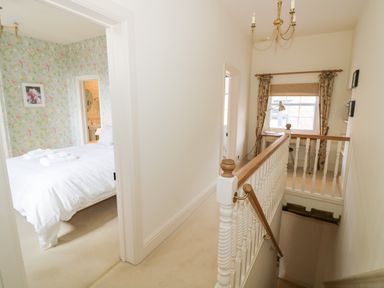 A hallway with a staircase and a bedroom with floral wallpaper and a bed with towels at 4 The Old Council House in Shipston-On-Stour