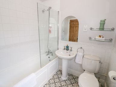 A bathroom with a bathtub and shower curtain a pedestal sink a toilet and shelves with towels and a vase at 4 The Old Council House in Shipston-On-Stour