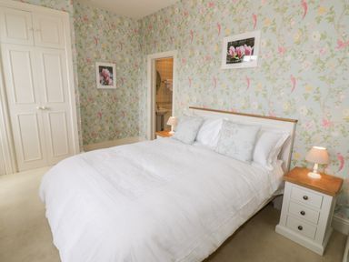 A bedroom with a white bed and floral wallpaper at 4 The Old Council House in Shipston-On-Stour