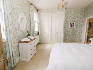 A bedroom with floral wallpaper a white dresser with towels a bed and built in closets at 4 The Old Council House Shipston-On-Stour