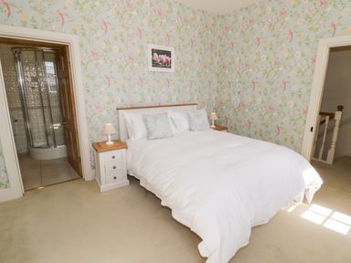 A bedroom with a double bed between two bedside tables with lamps and an en suite bathroom at 4 The Old Council House in Shipston-On-Stour