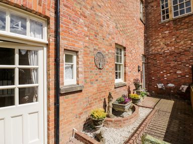 A brick patio with potted plants a small table with chairs and a door numbered 4 at 4 The Old Council House in Shipston-On-Stour