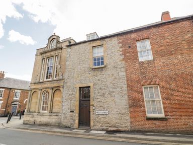 Stone and brick buildings with windows and a wooden door on a street corner with a West Street sign at 4 The Old Council House in Shipston-On-Stour