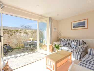 A living room with striped sofas a wooden coffee table and open doors leading to a patio with outdoor furniture at Smugglers Cove 7 in Beadnell