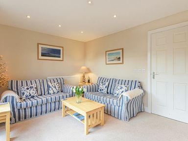 A living room with two striped sofas and a wooden coffee table with flowers at Smugglers Cove 7 in Beadnell