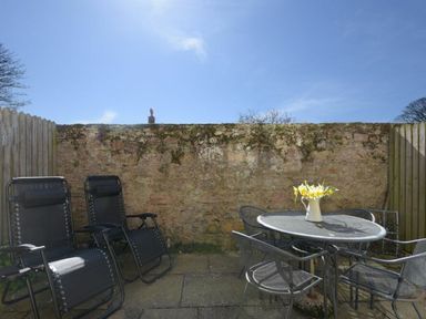 An outdoor patio with two black reclining chairs a round metal table with four chairs and a vase with flowers at Smugglers Cove 7 in Beadnell