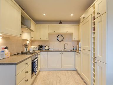 A kitchen with cream cabinets, countertop appliances, a sink, and a wall clock at Smugglers Cove 7 in Beadnell