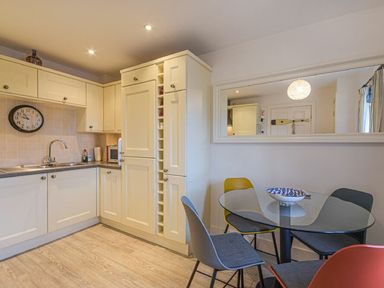 A kitchen with cream cabinets a round glass dining table with four chairs at Smugglers Cove 7 in Beadnell