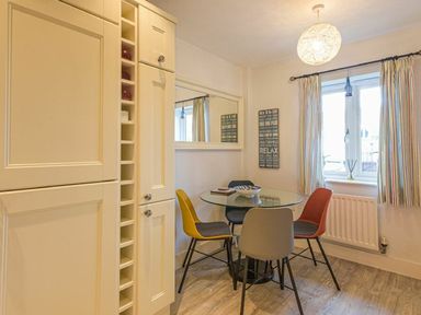 A dining area with a round glass table and four chairs next to a window with striped curtains at Smugglers Cove 7 in Beadnell