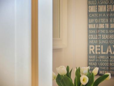 A vase with white tulips by a wall with a blue sign with text at Smugglers Cove 7 Beadnell