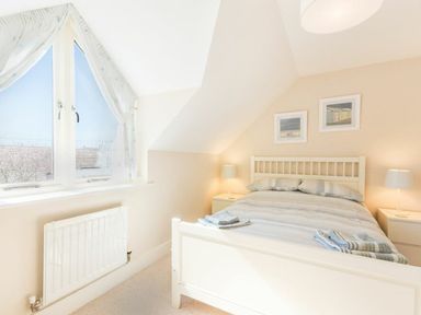 A bedroom with a bed two bedside tables with lamps a window with curtains and two framed pictures on the wall at Smugglers Cove 7 in Beadnell