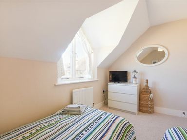 A bedroom with a striped bedspread a white chest of drawers a small TV an oval mirror and a window at Smugglers Cove 7 in Beadnell