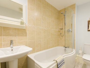 A bathroom with a white bathtub with a shower and a glass screen a white sink with a faucet and a toilet at Smugglers Cove 7 in Beadnell