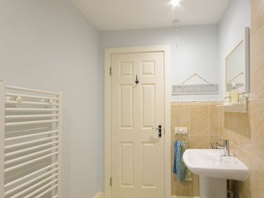 A bathroom with a door towel rack sink mirror and a beach house sign at Smugglers Cove 7 in Beadnell