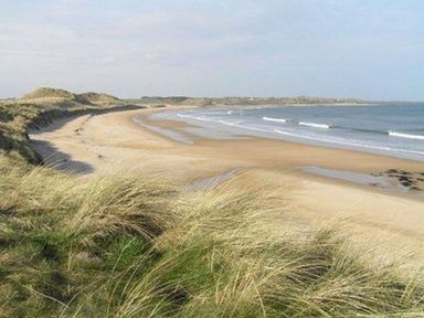 A sandy beach with grassy dunes and waves at Smugglers Cove 7 in Beadnell