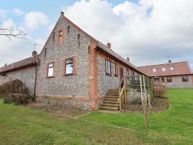 A stone and brick building with wooden stairs and green grass at Timbers in Weybourne