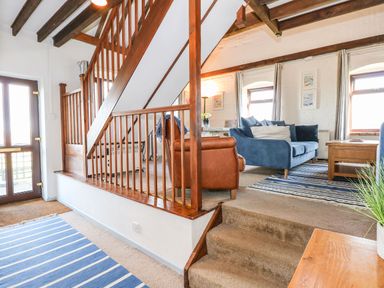 An interior room with wooden staircase blue sofas a brown armchair striped rugs and windows at Timbers in Weybourne