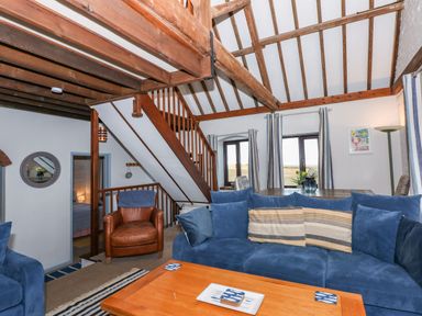 A living room with a blue sofa brown armchair wooden coffee table and visible wooden beams at Timbers in Weybourne
