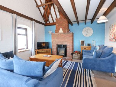 A living room with blue sofas a brick fireplace a wooden coffee table and a TV at Timbers in Weybourne
