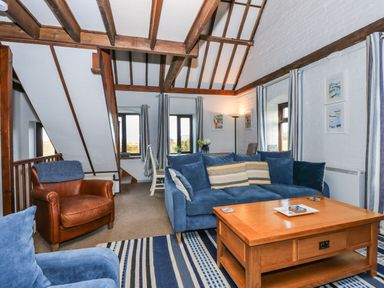A living room with blue sofas a wooden coffee table a leather armchair striped curtains and exposed wooden beams at Timbers in Weybourne