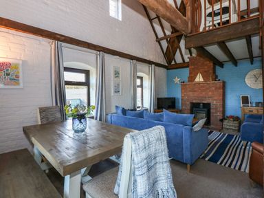 A living room and dining area with a wooden table a blue sofa a brick fireplace and exposed wooden beams at Timbers in Weybourne
