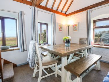 A dining area with wooden table chairs and bench by windows with striped curtains at Timbers in Weybourne