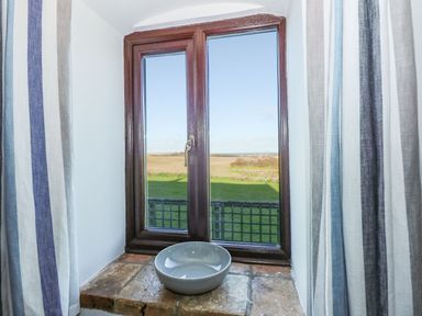 A closed wooden framed window with striped curtains and a ceramic bowl on the stone windowsill at Timbers in Weybourne