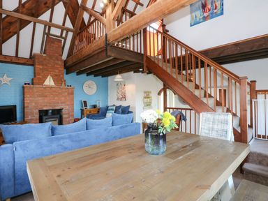 A living room with blue sofas a brick fireplace wooden stairs and a wooden table with flowers at Timbers in Weybourne