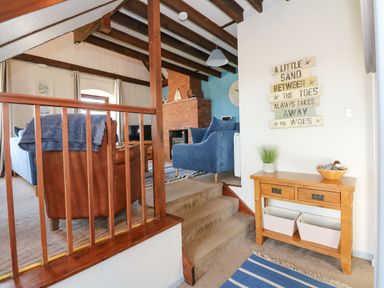 A living room with wooden ceiling beams blue sofa brown leather chair brick fireplace and a wooden console table with plants at Timbers in Weybourne