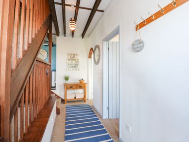 A hallway with wooden staircase a blue and white striped rug and a small wooden table at Timbers in Weybourne