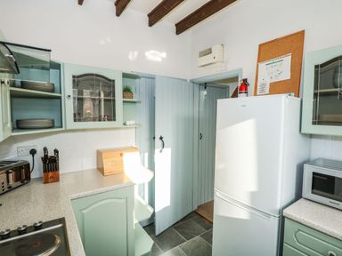 A kitchen with green cabinets a white refrigerator a microwave a toaster and knives at Timbers in Weybourne
