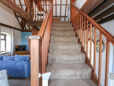 A carpeted staircase with wooden railings leading to an upper floor in a living area with a blue sofa and a television at Timbers in Weybourne