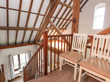 An upper level with two white chairs and a wooden railing overlooking stairs with exposed wooden beams at Timbers in Weybourne