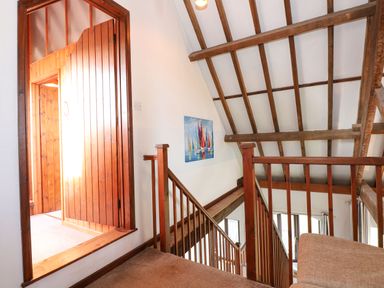 A staircase with wooden railings and beams with a wooden door and a painting of sailboats on the wall at Timbers in Weybourne