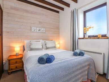 A bedroom with a bed with pillows and folded towels on a blanket with lamps on wooden bedside tables at Timbers in Weybourne