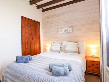 A bedroom with a bed made with striped blankets and rolled towels with wooden doors and nightstand at Timbers in Weybourne