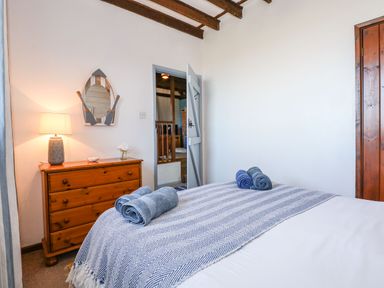 A bedroom with a bed covered by a patterned blanket and rolled towels a wooden chest of drawers with a lamp and a decorative mirror on the wall at Timbers in Weybourne
