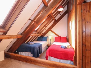 A bedroom with two single beds under a sloped wooden ceiling at Timbers in Weybourne