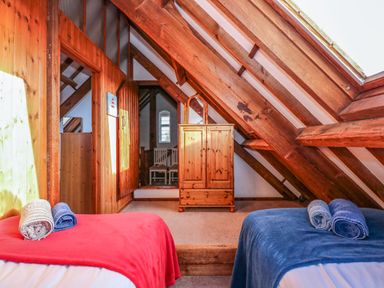 An attic bedroom with two beds covered with red and blue blankets and wooden beams at Timbers in Weybourne