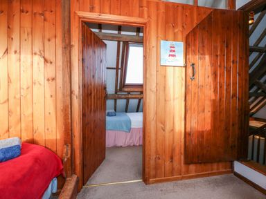 A wooden wall with two open doors showing a bedroom with a bed and a skylight window at Timbers in Weybourne