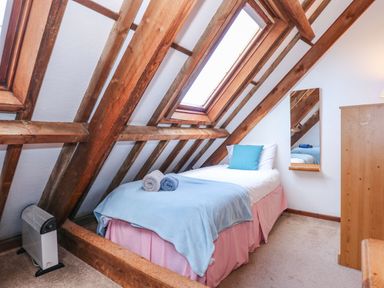 A single bed with blue and gray towels and a blue pillow under a skylight window in an attic bedroom at Timbers in Weybourne