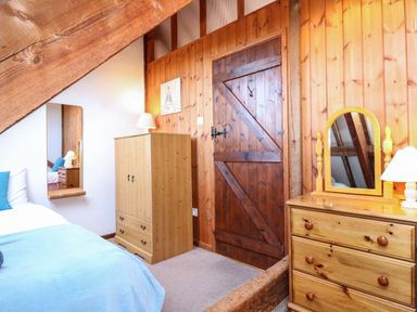 A bedroom with wooden furniture a bed with blue bedding a mirror on the wall and a wooden door at Timbers in Weybourne